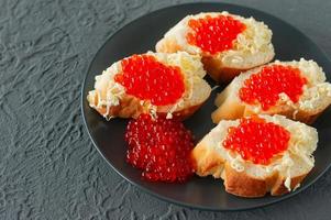 sanduíches com caviar vermelho, limão e salsa na chapa preta sobre fundo de concreto. frutos do mar. foto