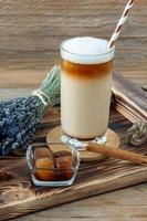 café com leite ou cappuccino com espuma de leite e lavanda em um copo alto na bandeja de madeira