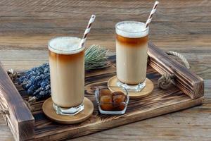café com leite ou cappuccino com espuma de leite e lavanda em um copo alto na bandeja de madeira