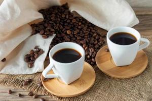duas xícaras de café expresso fresco na mesa de madeira. grãos de café na mesa de madeira clara, estilo rústico, caseiro. foto