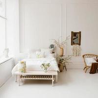 uma cama no quarto com lençóis brancos, flores amarelas da primavera em um vaso na mesa de cabeceira no interior branco do quarto foto