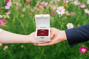 alianças de casamento em uma caixa nas palmas das mãos dos noivos em um fundo de flores foto