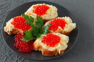 sanduíches com caviar vermelho, limão e salsa na chapa preta sobre fundo de concreto. frutos do mar. foto