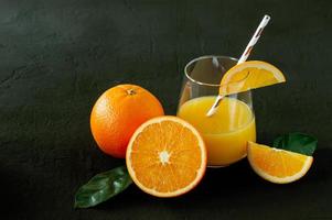 copo de suco de laranja fresco com frutas frescas em fundo preto foto
