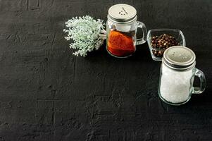 abanadores de vidro de pimenta e sal em um background de concreto preto com espaço de cópia foto