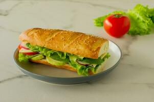 Sanduíche vegano de baguete longa integral com alface, abacate, tomate e queijo. lanche saudável e comida para viagem foto