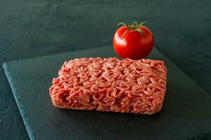 carne picada crua em uma ardósia com tomate. foto