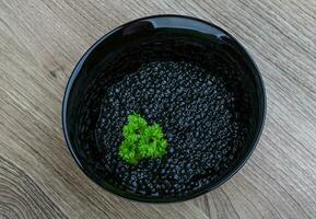 caviar preto em uma tigela sobre fundo de madeira foto