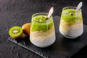 pudim de chia com kiwi, banana e manga. café da manhã de desintoxicação de saúde em copos no fundo de pedra preta foto