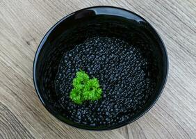 caviar preto em uma tigela sobre fundo de madeira foto