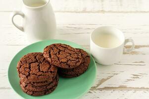 biscoitos de chocolate no café da manhã com um copo de leite em uma mesa de madeira branca. foto