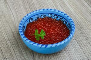 caviar vermelho em uma tigela sobre fundo de madeira foto