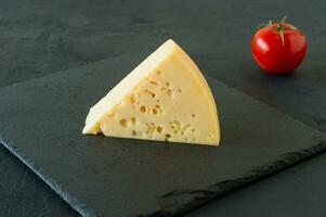 queijo radamer em um fundo preto de concreto. pedaço triangular de queijo suíço de leite de vaca amarelo com buracos foto