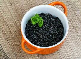 caviar preto em uma tigela sobre fundo de madeira foto