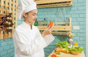 mulher asiática com uniforme de chef está cozinhando na cozinha. foto