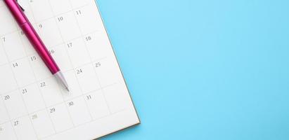 página do calendário com caneta close-up no conceito de reunião de compromisso de planejamento de negócios de fundo azul foto