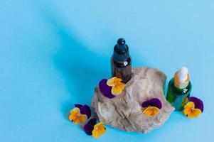 frascos de vidro de soro com pipeta e lindas flores de viola sobre fundo azul. conceito cosmético de spa orgânico natural. vista frontal. foto
