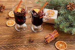 copos com vinho quente vermelho quente para o inverno e natal com fatia de laranja, anis e canela em pau decorado com ramos de abeto e presentes embrulhados para férias. cartão festivo foto