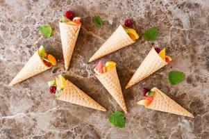 cones de frutas crocantes de waffle em uma mesa de mármore. doce sobremesa. postura plana foto