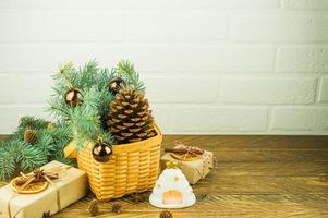 composição festiva de natal em uma mesa de madeira. cesta de vime com um grande cone de cedro, ramos de abeto, presentes e uma vela quente. foto