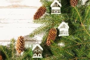 ano novo e decorações de natal em ramos de abeto. cones e brinquedos da floresta natural - casas cobertas de neve. fundo de madeira branco. vista do topo. foto