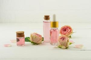 garrafas de vidro com tampa de cortiça e água de rosas, garrafa cosmética com óleo de rosas no contexto de botões de rosa e parede branca. cosméticos naturais. foto