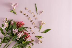 uma composição festiva para o dia das mães de lindas flores da primavera e inscrições em letras de madeira. fundo rosa. vista do topo. foto