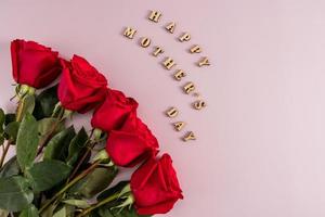 feliz dia das mães - escrito em letras de madeira em um fundo rosa com um lindo buquê de rosas. estilo plano. vista do topo. foto