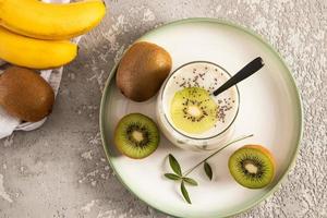 smoothie caseiro de kiwi e banana feito na hora com sementes de chia em um copo em uma bandeja de cerâmica e fundo de concreto. vista do topo. limpeza do corpo. foto