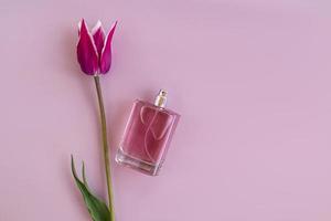 um frasco transparente de perfume feminino em um fundo roxo com uma flor de tulipa. vista do topo. um espaço de cópia. o conceito de publicidade da fragrância. foto