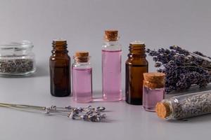 um conjunto de produtos cosméticos com extrato de flores de lavanda em vários frascos de vidro para autocuidado natural. fundo cinza. foto