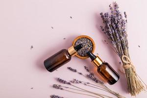 cosméticos da natureza em garrafas de vidro com uma pipeta e raminhos de lavanda em um fundo roxo. o conceito de cuidados com a pele e beleza. vista do topo. foto