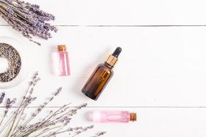 composição de produtos cosméticos naturais de flores e sementes de lavanda. soro ou óleo em garrafas de vidro em um fundo branco de madeira. vista do topo. foto