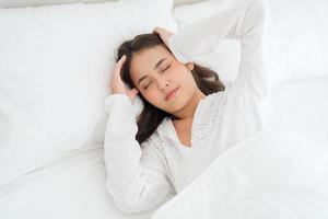 menina deitada na cama doente sofre de insônia dor de cabeça ansiedade, segurando sua cabeça foto