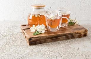 dois copos transparentes de vidro com chá de jasmim aromático em uma bandeja de madeira. bule de chá com chá acabado de fazer. hora do chá. foto