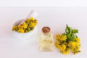 garrafa de vidro com tampa de cortiça com st. óleo de erva-de-joão. argamassa com flores da planta e pistilo. o conceito de óleo de cozinha em casa. foto