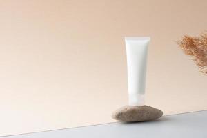 tubo branco de creme cosmético em um pódio de pedra com pampas em fundo bege. feche, copie o espaço. foto