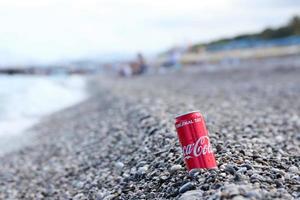 antalya, turquia - 18 de maio de 2021 lata vermelha original da coca cola encontra-se em pequenas pedras redondas perto da costa do mar. coca-cola na praia turca foto