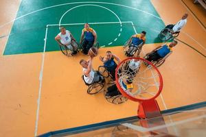 guerra com deficiência ou veteranos de trabalho mistos de raça e idade equipes de basquete em cadeiras de rodas jogando uma partida de treinamento em um ginásio de esportes. conceito de reabilitação e inclusão de pessoas com deficiência. foto