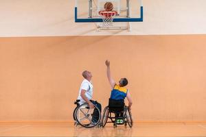 Veteranos de guerra com deficiência equipes de basquete de raça mista e idade em cadeiras de rodas jogando uma partida de treinamento em um ginásio de esportes. conceito de reabilitação e inclusão de pessoas com deficiência foto