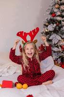 menina loira feliz em casa de pijama para o natal classificando presentes e brincando com brinquedos de natal foto