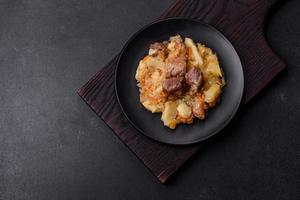 delicioso ensopado de legumes com carne, batatas, cenouras e repolho em um prato preto foto