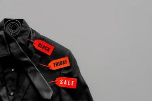 postura plana de camisa de cor preta masculina, terno, gravata e etiquetas de preço vermelhas em fundo cinza para o conceito de venda de sexta-feira negra. foto