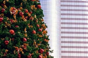 a árvore de natal decora com muitos ornamentos que tem um edifício alto em segundo plano para o festival de férias de natal. foto