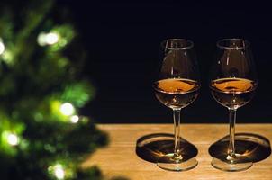 dois copos de vinho rosé na mesa de madeira com árvore de natal e fundo escuro. foto