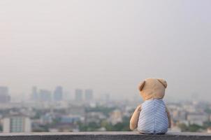 urso de pelúcia solitário sentado no telhado do prédio e olhando para a vista da cidade. foto
