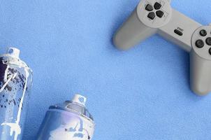 adolescentes e conceito de estilo de vida da juventude. joystick e duas latas de spray estão no cobertor de tecido de lã azul peludo. controladores para videogames e latas de tinta em um fundo de material de lã de pelúcia foto