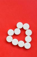 vários comprimidos brancos estão sobre um fundo vermelho brilhante em forma de coração. imagem de fundo sobre medicina e tópicos farmacêuticos foto