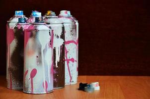 natureza morta com um grande número de latas de spray coloridas usadas de tinta aerossol na superfície de madeira tratada na oficina de grafite do artista. latas sujas e manchadas para arte em spray foto