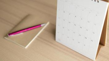 página do calendário fechar no fundo da mesa de madeira com conceito de reunião de compromisso de planejamento de negócios de caneta e caderno foto